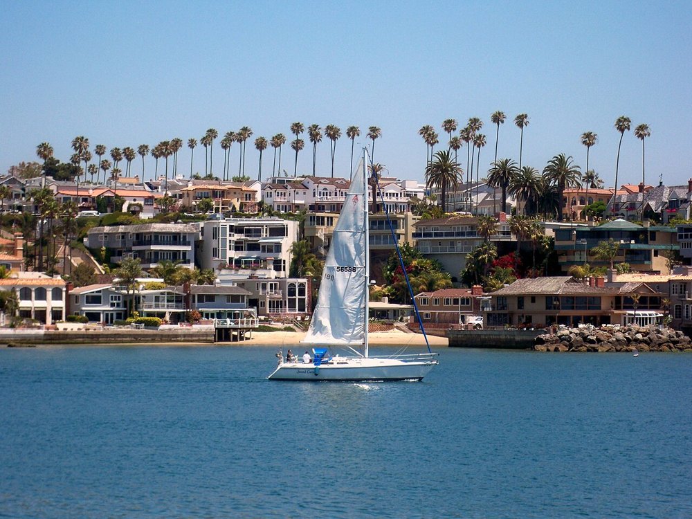 A sailboat passing the Balboa Island waterfront